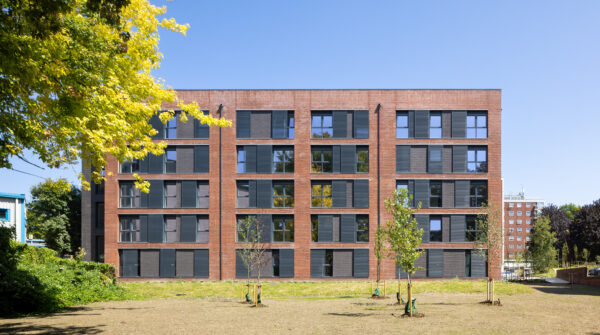 Modern brick residential building with large windows, set within landscaped green space, representing strong partnerships, fair working practices, and long-term collaboration across the supply chain.